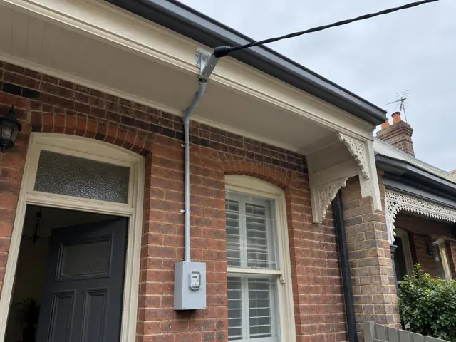 Overhead service cable and point-of-attachment bracket on a brick house facade with meter box in Leichhardt